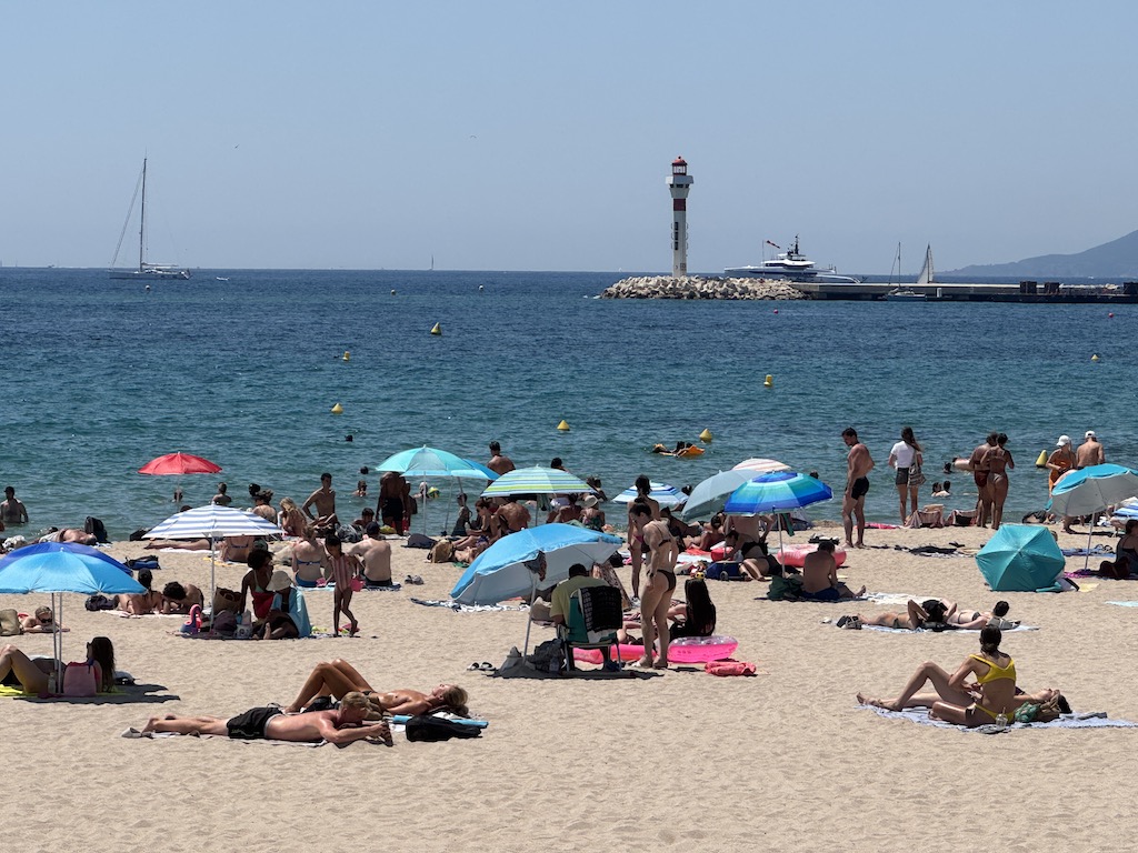 Plage du Midi - Arka planda görünen ikonik deniz feneri (Phare du Vieux Port), Cannes Eski Limanı'nın (Vieux Port) dalgakıranı üzerinde yer alıyor. Fotoğrafın sağ tarafındaki tepelik alansa Estérel Dağları'nın (Massif de l'Estérel) silüeti.